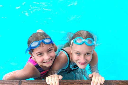 Smiling girls sisters wearing swimming goggles in a clear outdoor pool, enjoying summer vacation together. Happy childhood, family leisure, healthy lifestyle and fun water activities.