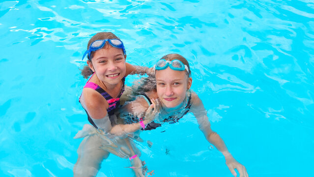 Happy sisters in swimming goggles swim in a clean outdoor pool, enjoying their summer vacation together. A happy childhood, family vacations, a healthy lifestyle, and fun water activities.