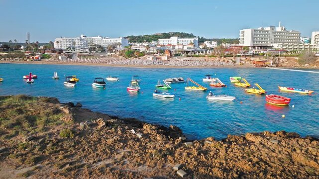 Aerial view of Fig Tree Beach in Protaras, Cyprus. Clear blue water, sandy beach, beachfront hotels and colorful water sports boats create a lively Mediterranean summer holiday scene.