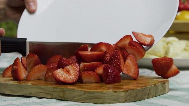 Slow motion shot of diced strawberries being moved back onto chopping board