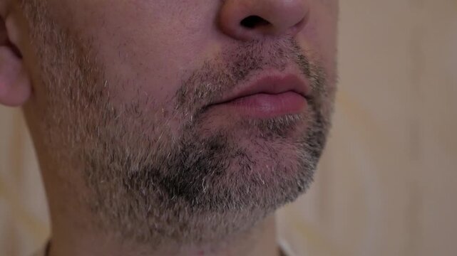 An adult man pulls down his lower lip with fingers indoors to inspect his lower teeth and gums for dental issues.
