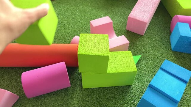 Adult hand building a tower with large colored blocks, educational play, creative construction, child development concept.