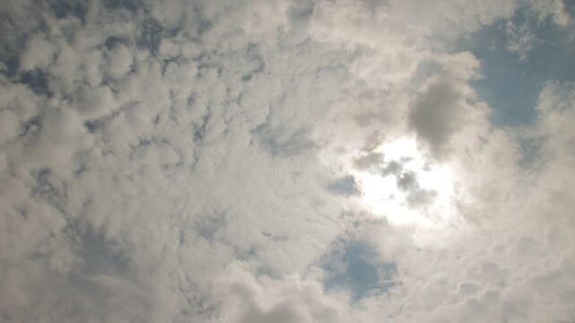 Time-lapse of bright sun shining through a textured layer of moving white and gray clouds