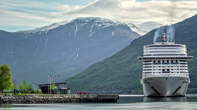 View of a large cruise ship docked at the pier in Flam with snow-capped mountains in the background in Flam, Vestland, Norway.