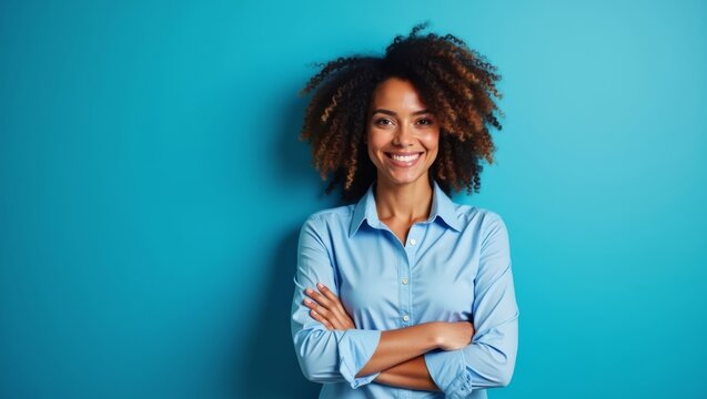 Smiling African American woman with curly hair wearing a light blue shirt stands confidently with arms crossed against a solid turquoise background