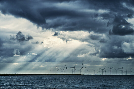Wind turbines standing in water under dramatic dark clouds, generating clean renewable energy
