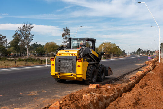 Rear view of yellow skid steer loader parked on the edge of newly paved highway