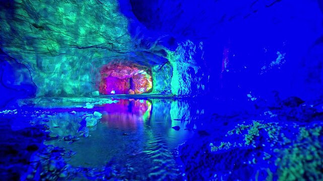 View of the illuminated cave interior with vibrant colorful lights reflecting on the calm water surface in Flam, Vestland, Norway.