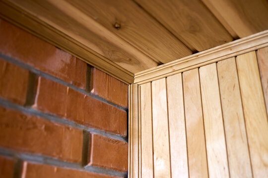 Sauna interior corner details showing wooden lining texture combined with red brick wall structure. Natural yellow timber planks cover ceiling and walls completed with classic design crown molding.