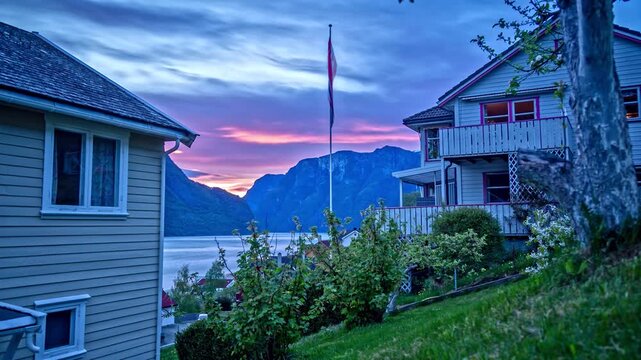 View of traditional wooden houses in Flam with mountains and a fjord at sunset in Flam, Vestland, Norway.