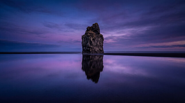 Solitary Weathered Sea Stack Reflected on Mirror-Like Black Sand Beach During Deep Purple Twilight