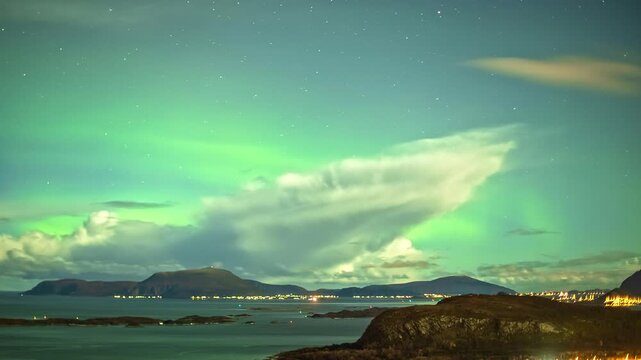 View of vibrant green Northern Lights illuminating the night sky above the coastal town of Alesund, More og Romsdal, Norway.