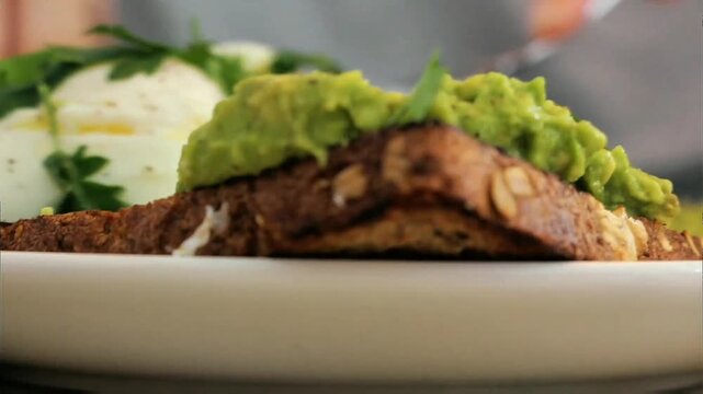 Thick toasted whole grain bread topped generously with smooth creamy green avocado spread, soft focus fresh side dish in background