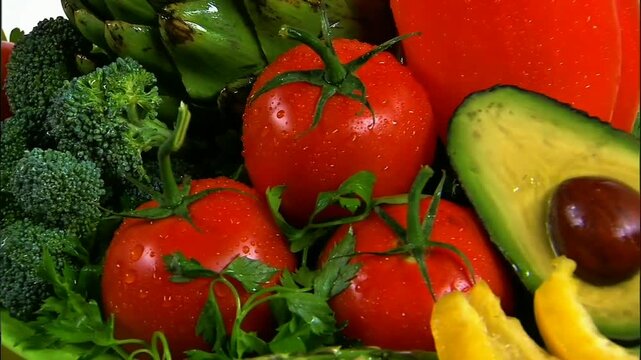 Vibrant fresh vegetables glistening with tiny water droplets: red ripe tomatoes, green broccoli, avocado, artichoke and parsley sprigs