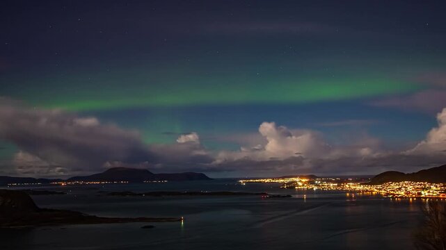View of the vibrant green aurora borealis illuminating the night sky above the illuminated coastal town of Alesund, More og Romsdal, Norway.