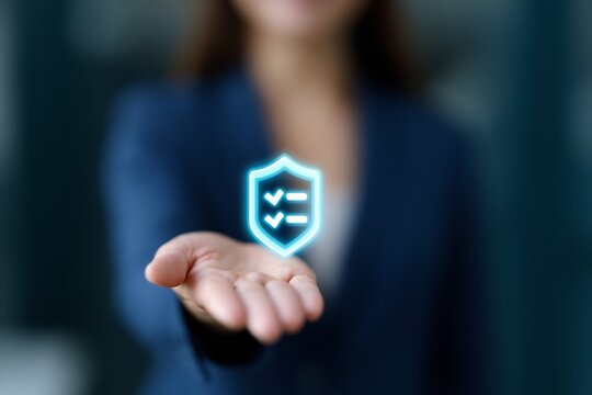 A person's hand holding a glowing blue shield icon with checkmarks, symbolizing security and protection.
