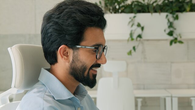 Glad happy Indian Arabian business man smiling work laptop indoor corporate office success project male entrepreneur businessman boss working online typing browsing internet computer programming deal