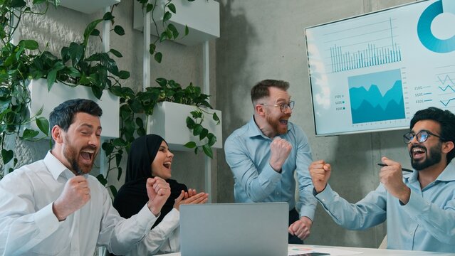 Happy multiethnic business team celebrating victory success laptop office coworkers win deal finance Arabian Indian Caucasian men muslim woman in hijab teamwork achievement corporate workplace indoor