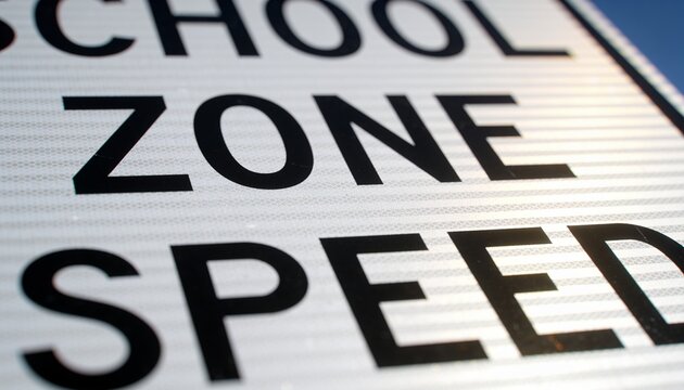 Displaying reflective road sign showing partial SCHOOL ZONE SPEED text at roadside, beaded texture