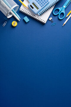 Back to school flat lay with blue stationery, notebook, calculator, pencils and scissors on vertical dark blue backdrop with copyspace for text