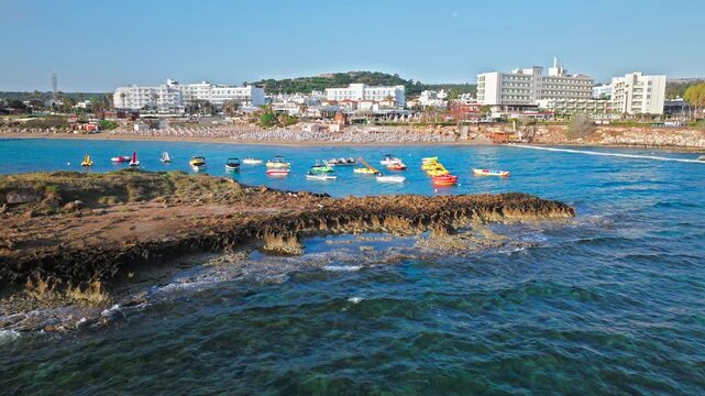 Aerial view of Fig Tree Beach in Protaras, Cyprus. Clear turquoise water, rocky shoreline and anchored boats create a bright coastal holiday scene