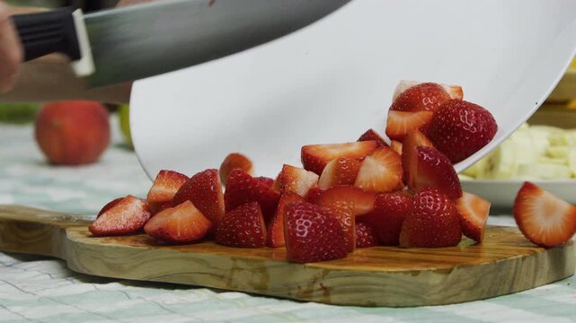 Chef using sharp knife to push diced strawberries onto chopping board - closeup slow motion shot