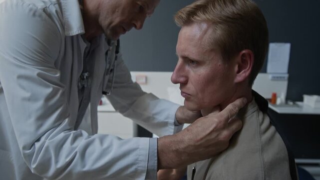 Caucasian middle aged doctor palpating neck of Caucasian young male patient during medical examination. Clip for healthcare marketing and clinical services promotion