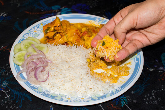 a bite of mixed rice and sabji in hand, eating homemade lunch at table. 