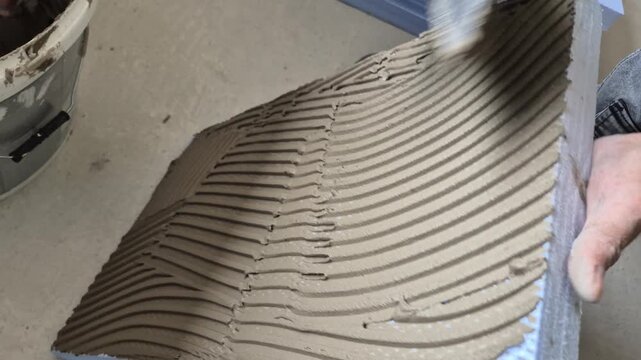 Close up shot of a worker applying cement-based adhesive onto an extruded polystyrene (XPS) foam board using a putty knife.
