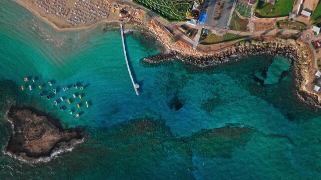 Drone view of Fig Tree Beach in Protaras, Cyprus. A wider coastal perspective shows the beach, small offshore boats and the scenic shoreline from above.