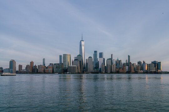 View of the New York City skyline featuring One World Trade Center rising above the skyscrapers along the Hudson River at sunset in New York, New York, United States.
