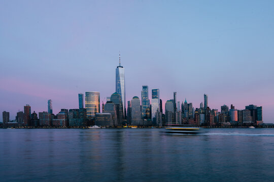 View of the One World Trade Center and the Manhattan skyline across the Hudson River at dusk with a soft pink and blue sky in New York, New York, United States.