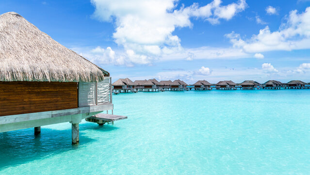 View of overwater bungalows with thatched roofs situated over the turquoise lagoon in Bora-Bora, Leeward Islands, French Polynesia.