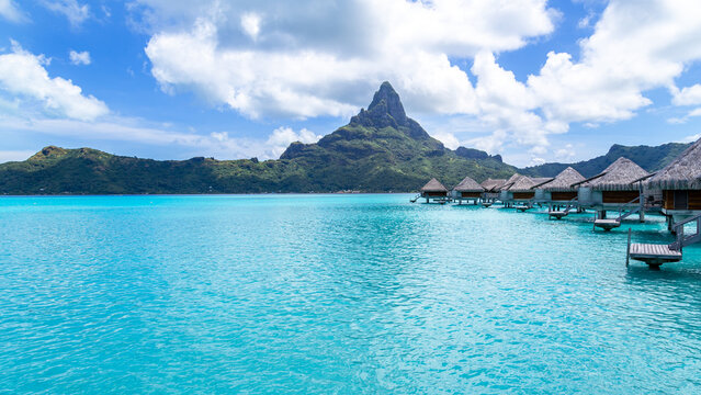 View of overwater bungalows over a turquoise lagoon with Mount Otemanu in the background in Bora-Bora, Leeward Islands, French Polynesia.