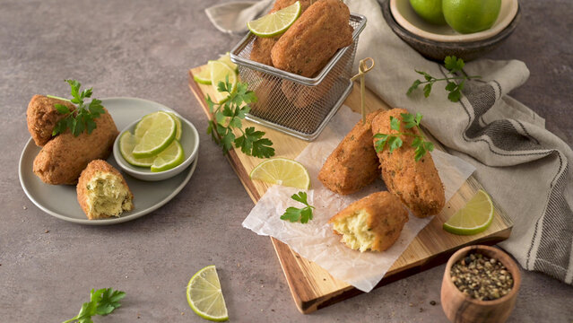Crispy fried codfish cakes served with fresh lime slices and parsley on a rustic wooden board and plate