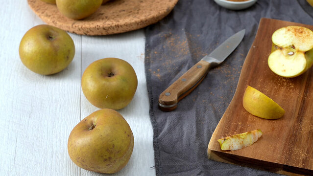 Fresh golden russet apples arranged on a white wooden table with a cutting board and a knife