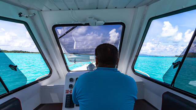 View of a boat captain steering through the turquoise waters of a tropical lagoon in Bora-Bora, Leeward Islands, French Polynesia.