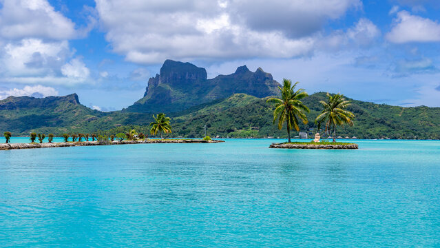 View of the turquoise lagoon and Mount Otemanu with palm trees on a small island in Bora-Bora, Leeward Islands, French Polynesia.