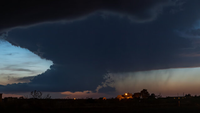 View of a massive dark storm cloud formation at dusk with rain shafts and dramatic lighting over the landscape in Oklahoma City, Oklahoma, United States.