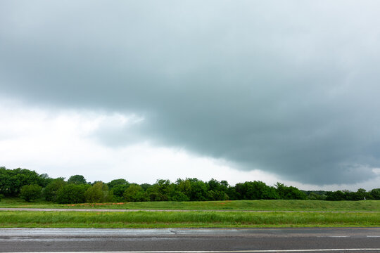 View of a dark, ominous storm cloud gathering over a green landscape and a road in Oklahoma City, Oklahoma, United States.