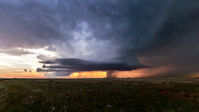 View of a dramatic supercell thunderstorm with dark, swirling clouds and rain curtains over the flat plains during sunset in Oklahoma City, Oklahoma, United States.