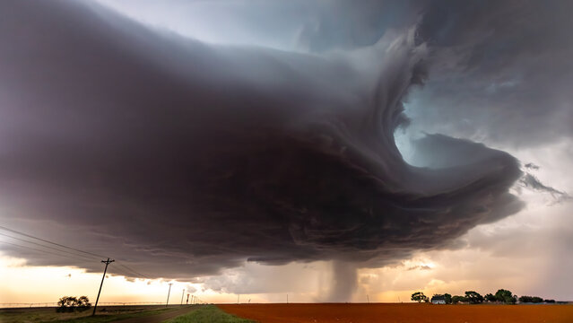 View of a massive supercell storm cloud with a rotating funnel over a rural field with power lines in Oklahoma City, Oklahoma, United States.