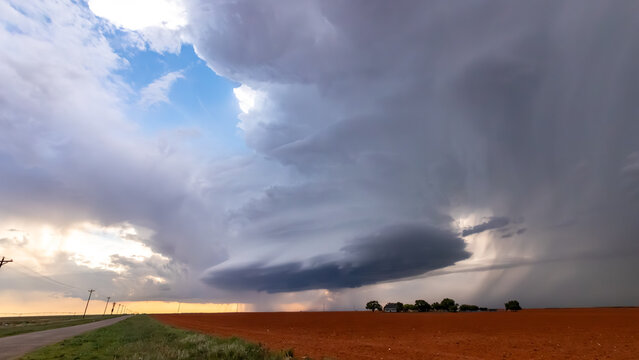 View of a dramatic supercell storm cloud hovering over a vast red dirt field in rural Oklahoma City, Oklahoma, United States.