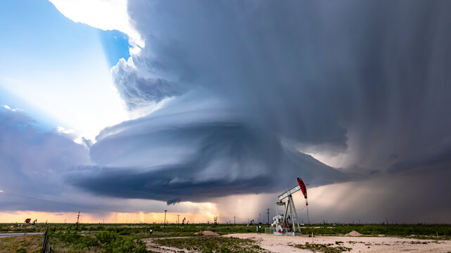 View of a dramatic supercell storm cloud looming over an oil pump jack in a vast field in Oklahoma City, Oklahoma, United States.
