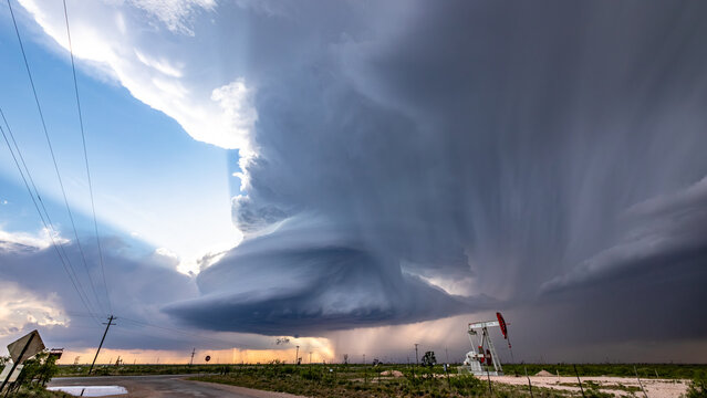 View of a dramatic supercell storm with dark, swirling clouds and rain shafts over a rural landscape featuring an oil pump jack and power lines in Oklahoma City, Oklahoma, United States.