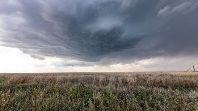 View of a dramatic supercell storm cloud looming over a vast, dry grassy field in Oklahoma City, Oklahoma, United States.