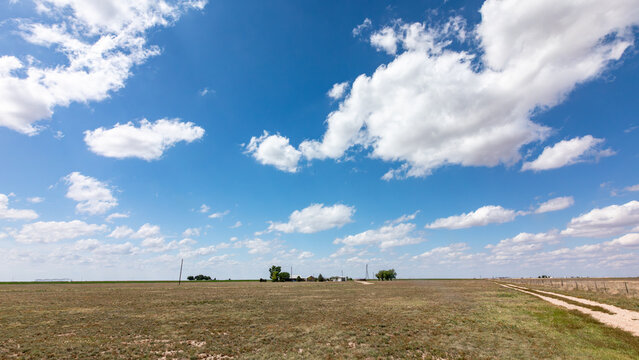 View of a rural landscape with a dirt road stretching through dry fields under a vast blue sky with scattered white clouds in Oklahoma City, Oklahoma, United States.