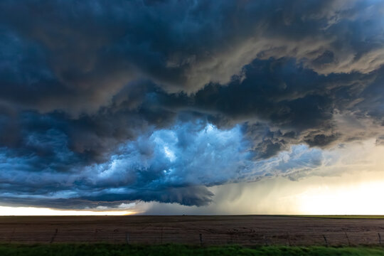 View of a dramatic supercell storm with dark, swirling clouds and heavy rain over a vast agricultural field in Oklahoma City, Oklahoma, United States.