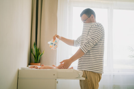 Father holding a dirty diaper while standing next to a changing table, changing his newborn baby's diaper, focusing on essential daily routine and responsibilities of new parenthood and infant care