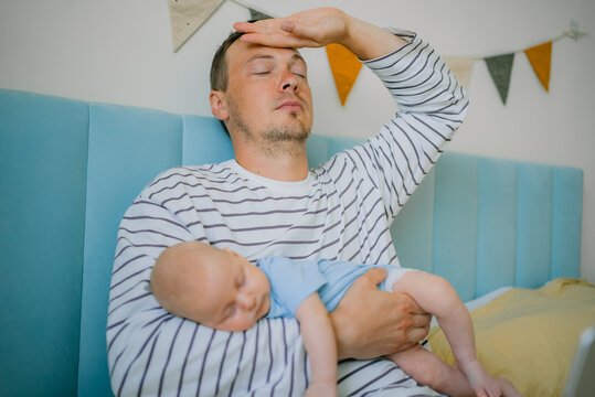 Overwhelmed new father holding his sleeping baby, feeling tired and experiencing the challenges of postpartum life and sleep deprivation while managing parental duties